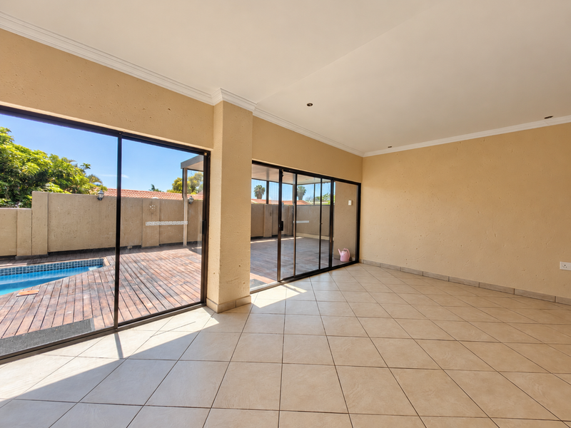 Spacious, empty living area featuring large sliding glass doors that open onto a wooden deck and swimming pool area.