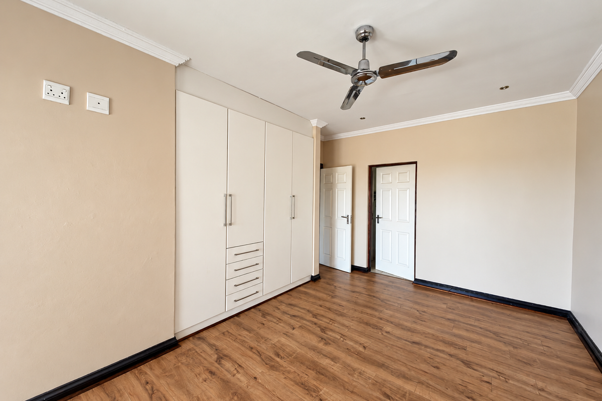 A spacious, empty bedroom featuring built-in cupboards, a ceiling fan, and modern laminate flooring with neutral wall tones.