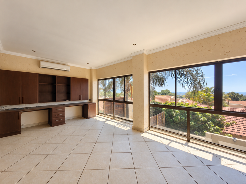Spacious home office featuring extensive built-in cabinetry, a dedicated desk area, tiled flooring, and large windows offering pleasant views.