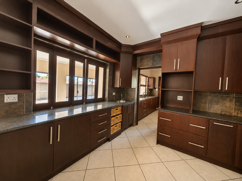 A spacious and well-appointed scullery featuring extensive dark wood cabinetry, granite countertops, tiled flooring, and a secondary sink area.