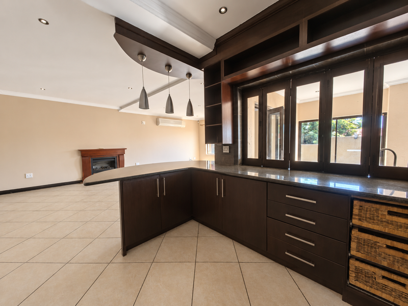 Spacious open-plan living area featuring a modern kitchen with dark wood cabinetry, granite countertops, tiled floors, a fireplace, and integrated air conditioning.