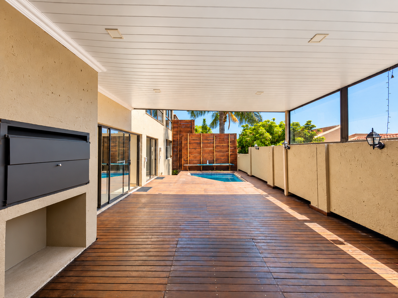 Spacious covered patio featuring timber decking, a built-in braai, and direct access to a private swimming pool area.