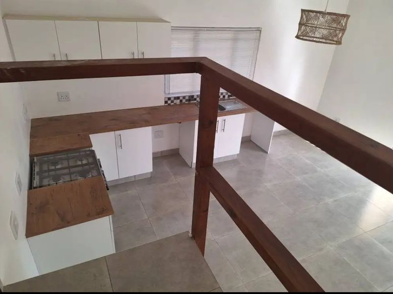 A clean, modern kitchen featuring white cabinetry, wood-look countertops, a gas hob, and tiled flooring, viewed from an elevated position behind a timber balustrade.