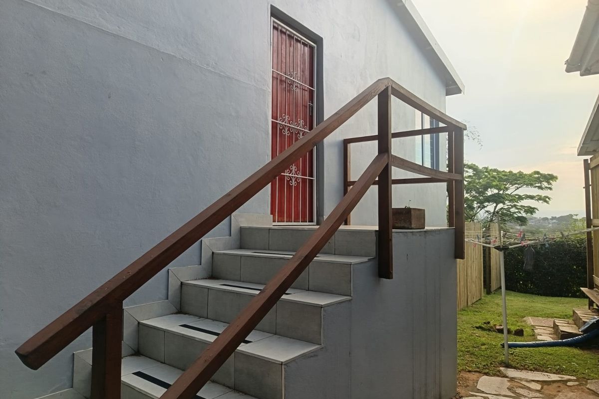 Rear exterior view of the property featuring a tiled staircase with a wooden handrail leading to a secure entrance door.