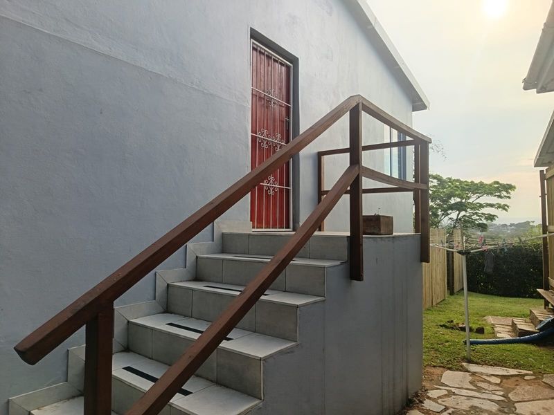 Rear exterior view of the property featuring a tiled staircase with a wooden handrail leading to a secure entrance door.