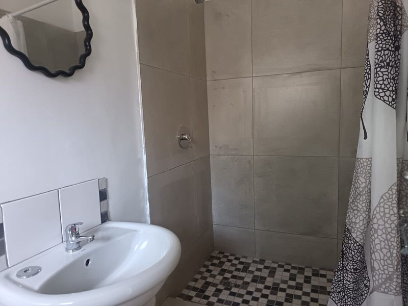 A functional bathroom featuring a pedestal basin with chrome mixer tap and a tiled shower enclosure with mosaic floor detailing.