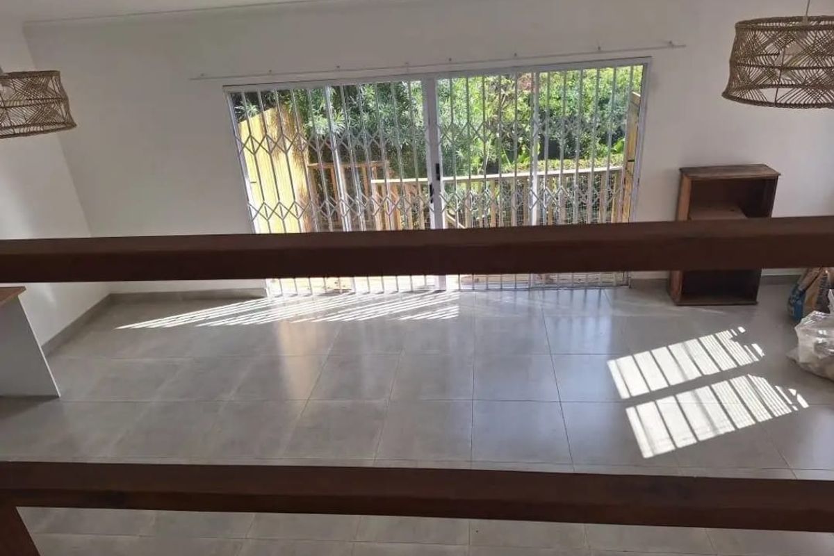Bright and spacious living area featuring neutral tiled flooring, a wooden balustrade, and sliding glass doors leading to an outdoor space.