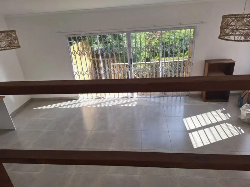 Bright and spacious living area featuring neutral tiled flooring, a wooden balustrade, and sliding glass doors leading to an outdoor space.