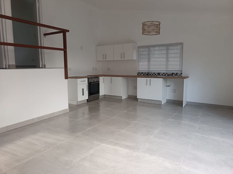 An open-plan kitchen and living area featuring tiled floors, white cabinetry with laminate countertops, and a freestanding stove, offering a clean, neutral space.