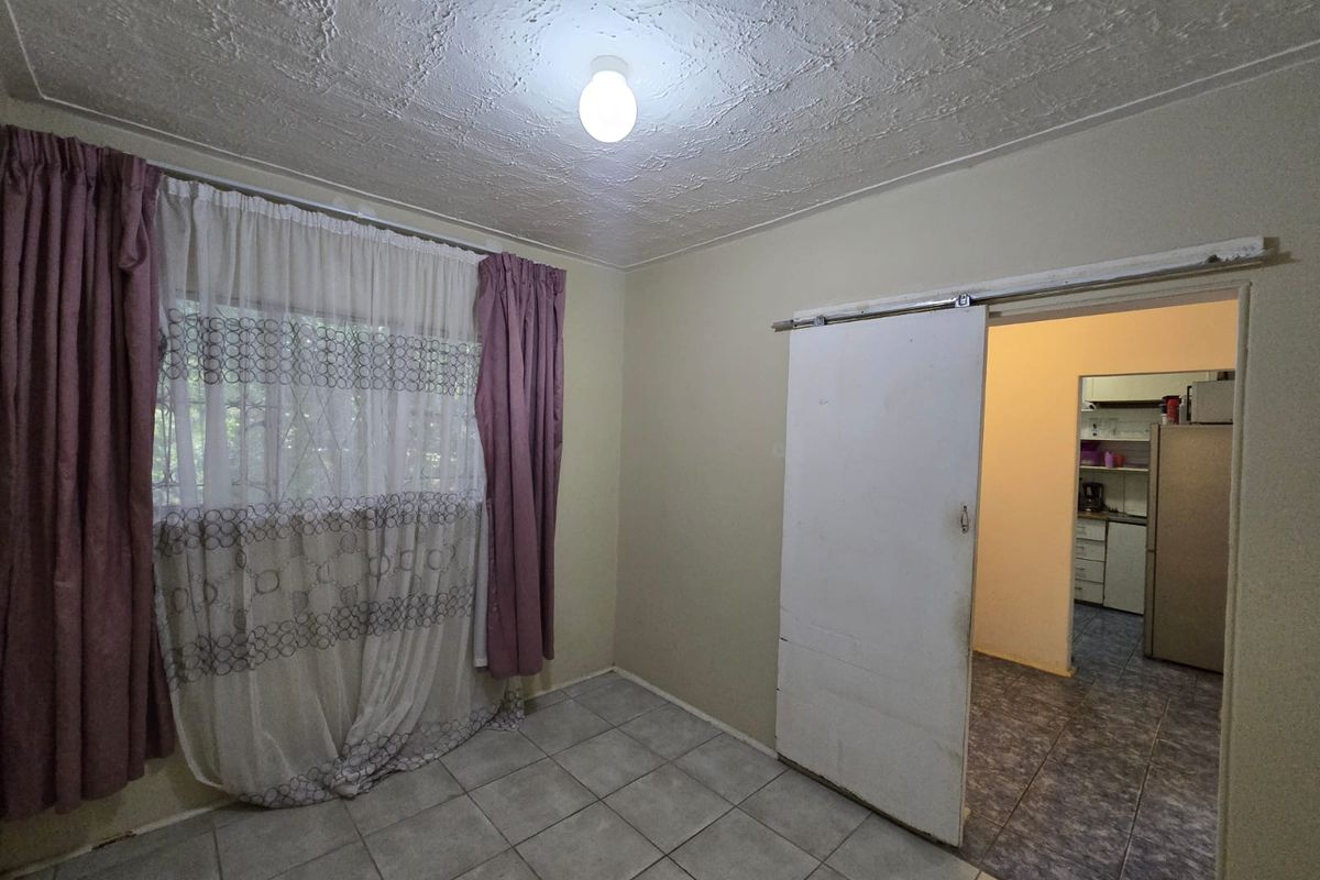 An empty living area featuring tiled flooring, a textured ceiling, and a sliding door providing access to the adjacent kitchen space.