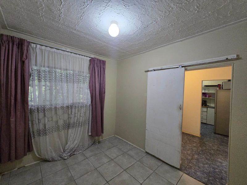 An empty living area featuring tiled flooring, a textured ceiling, and a sliding door providing access to the adjacent kitchen space.