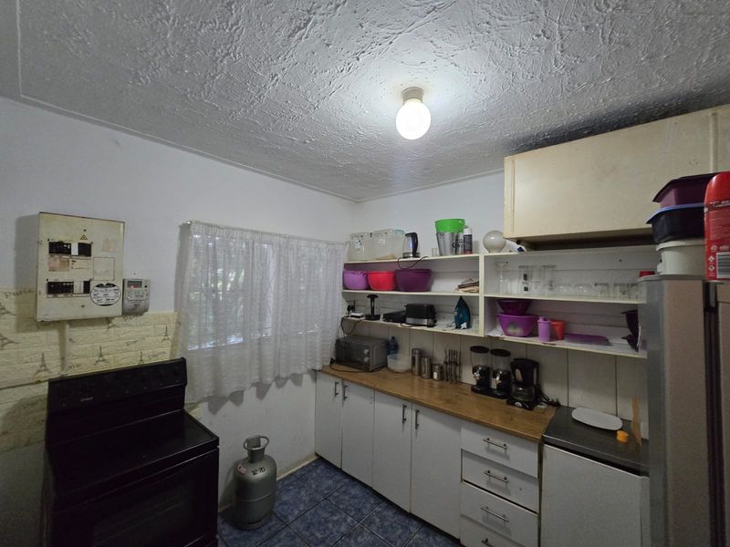 A functional kitchen featuring built-in cabinetry, open shelving, and tiled flooring, offering a practical layout with potential for modernization and cosmetic updates.