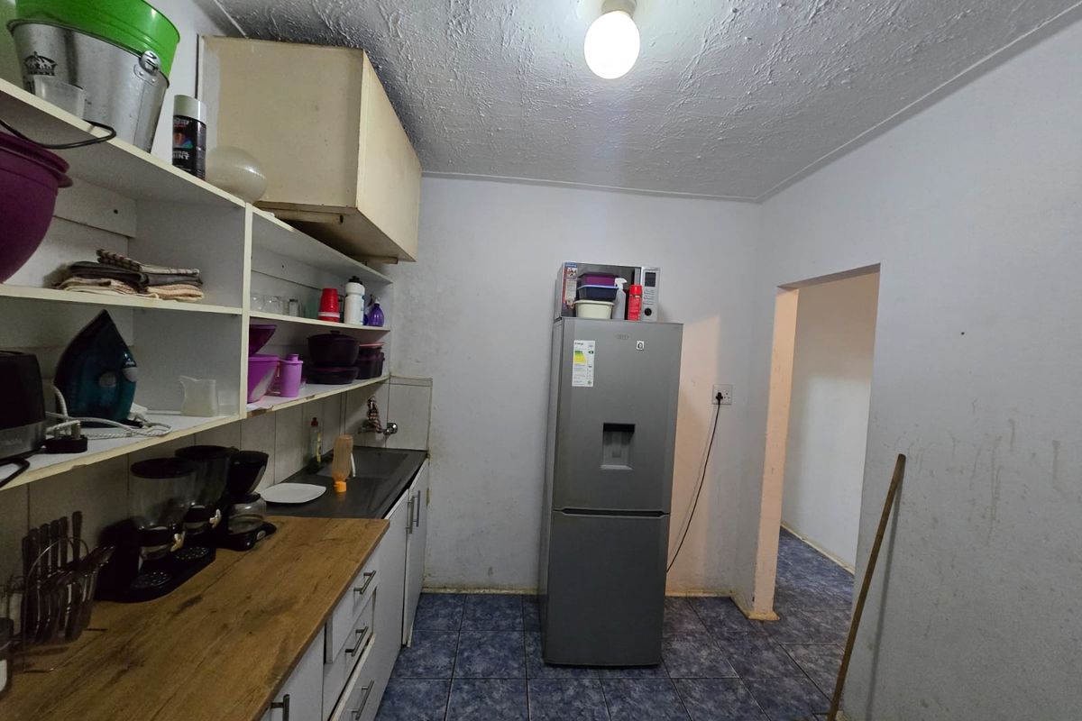 A functional kitchen area featuring built-in cabinetry, a laminate countertop, and tiled flooring, currently showing signs of wear and requiring cosmetic updates.