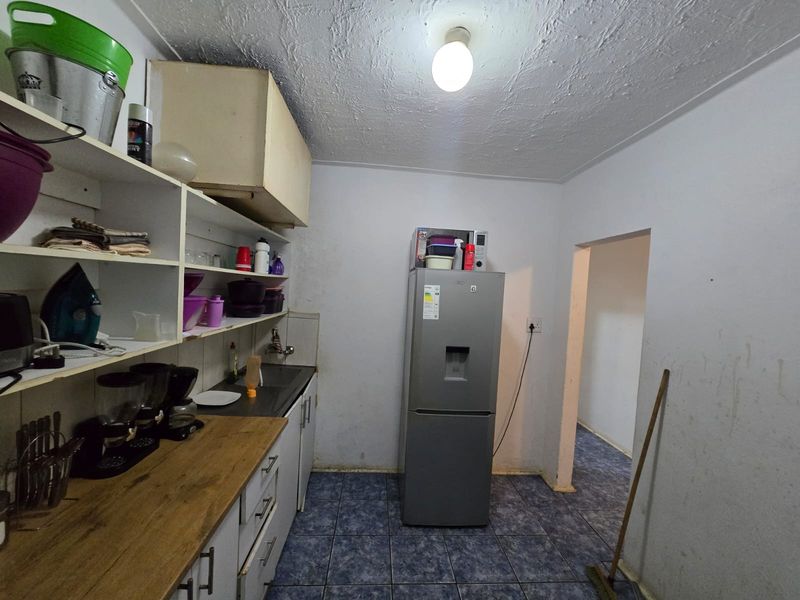 A functional kitchen area featuring built-in cabinetry, a laminate countertop, and tiled flooring, currently showing signs of wear and requiring cosmetic updates.