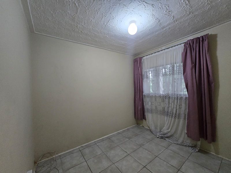 An empty bedroom featuring tiled flooring and a textured ceiling, offering a blank canvas for potential renovation and interior design updates.