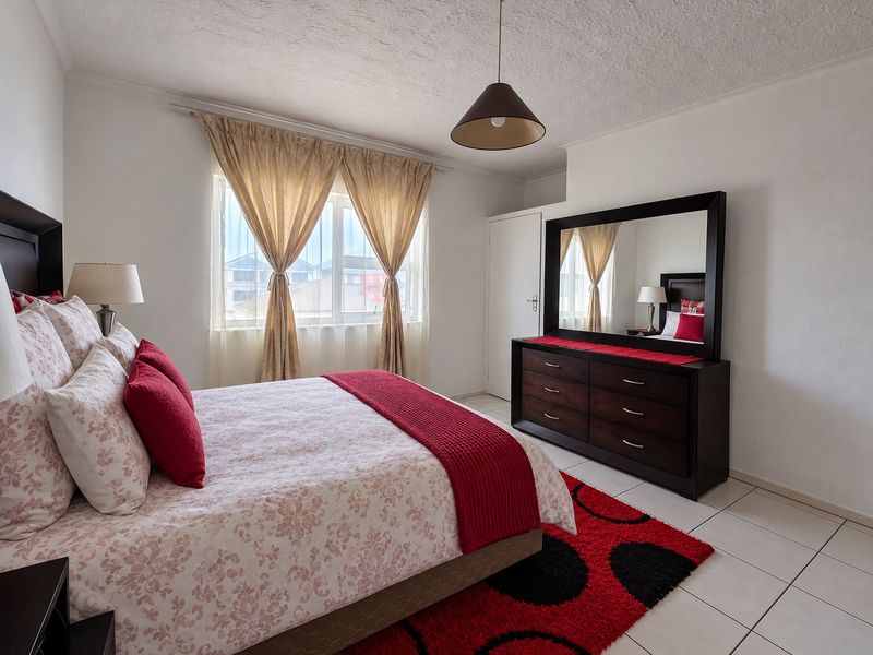 A well-maintained bedroom featuring tiled flooring, a built-in cupboard, and a central pendant light fixture, offering a functional and comfortable living space.
