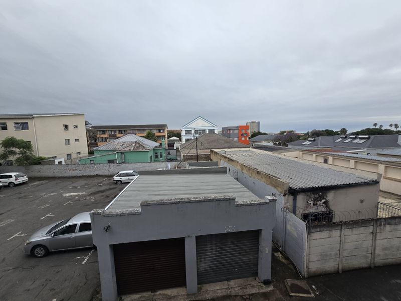 An elevated view overlooking the surrounding urban neighborhood, featuring various building rooftops, a parking area, and perimeter boundary walls.