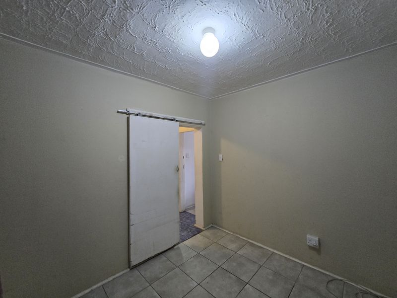 An empty bedroom featuring tiled flooring, a textured ceiling, and a sliding door leading to an adjacent space.