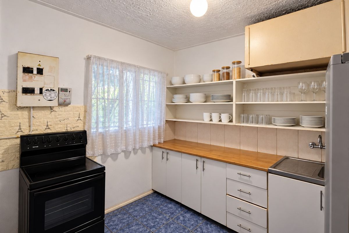 A functional kitchen featuring wooden countertops, open shelving, built-in cabinetry, and a freestanding stove, with tiled flooring and security bars on the window.