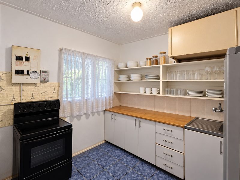 A functional kitchen featuring wooden countertops, open shelving, built-in cabinetry, and a freestanding stove, with tiled flooring and security bars on the window.