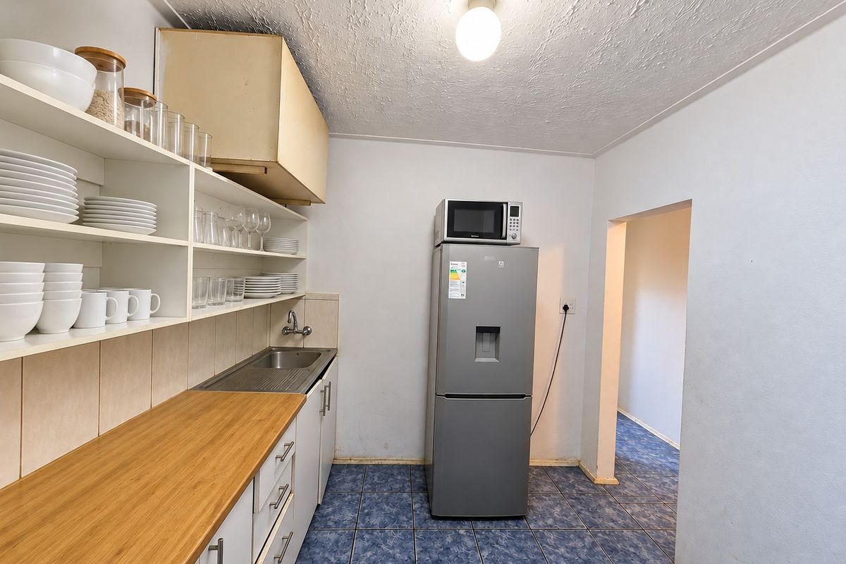 Functional scullery area featuring built-in cabinetry, a stainless steel sink, laminate countertops, and tiled flooring, providing practical utility space.