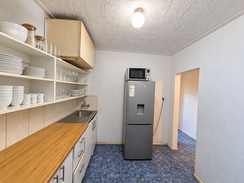 Functional scullery area featuring built-in cabinetry, a stainless steel sink, laminate countertops, and tiled flooring, providing practical utility space.
