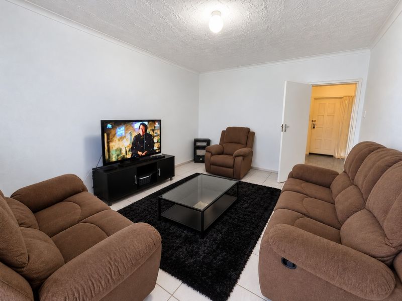 A neutrally painted living room featuring tiled flooring and coved ceilings, providing a functional and well-lit space with direct access to the entrance hallway.