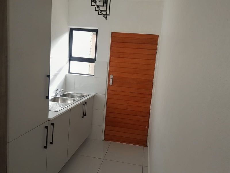 A clean and functional scullery featuring modern white cabinetry, a stainless steel double sink, tiled flooring, and a solid timber door.