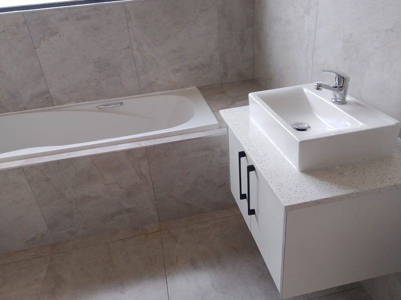 Modern bathroom featuring a built-in bathtub and a sleek wall-mounted vanity with a countertop basin and contemporary chrome fixtures.
