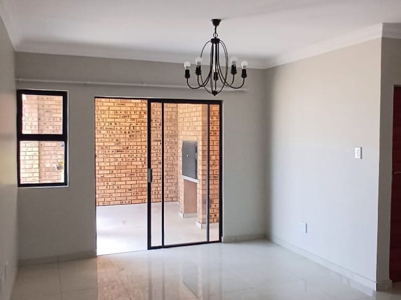 Spacious, light-filled living area featuring polished porcelain tiles, modern chandelier, and seamless access to an outdoor patio with a built-in braai.
