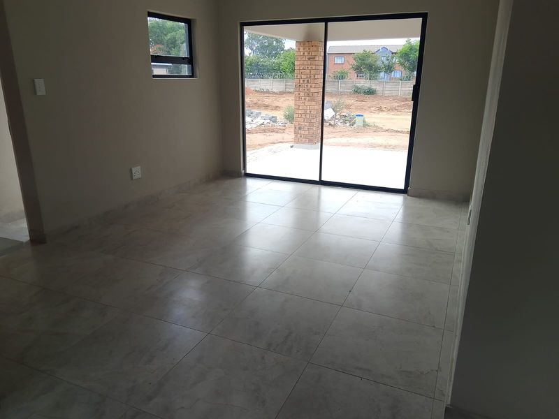 An empty, modern living area featuring neutral tiled flooring and a large sliding glass door providing access to the outdoor patio.