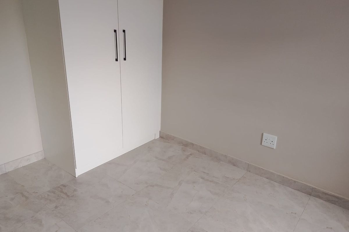 A clean, empty bedroom featuring neutral tiled flooring and a modern built-in wardrobe with sleek handles.