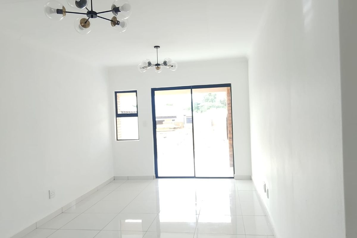 A bright, empty living room featuring polished white floor tiles, modern pendant lighting, and a large sliding glass door leading to the exterior.