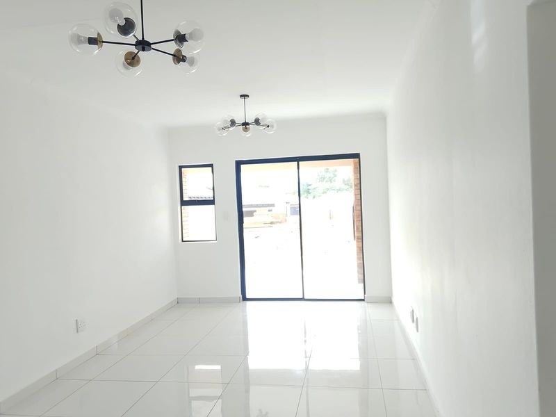 A bright, empty living room featuring polished white floor tiles, modern pendant lighting, and a large sliding glass door leading to the exterior.