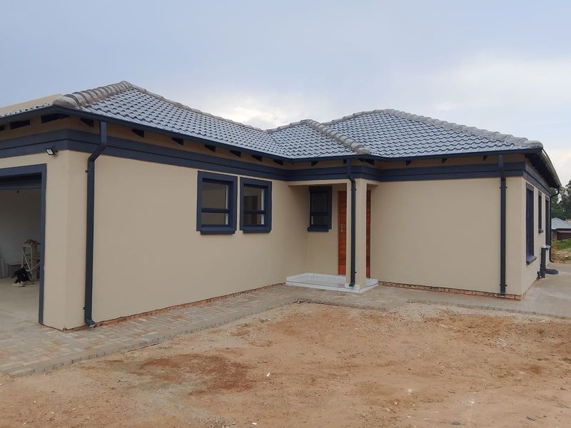 Modern single-story house exterior featuring a tiled roof, neutral painted facade, and paved walkway, currently awaiting final landscaping.