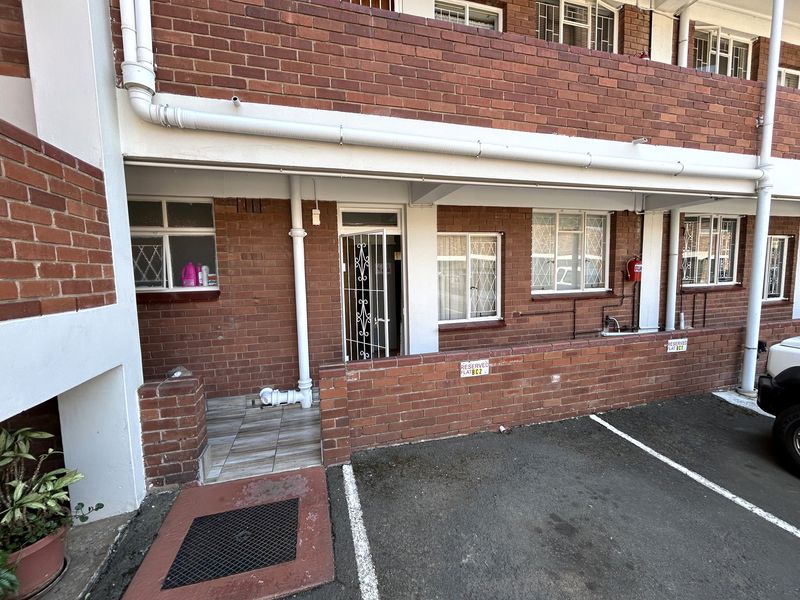 Front exterior view of a brick-faced flat featuring a private entrance with security gate, tiled threshold, and dedicated parking bay.