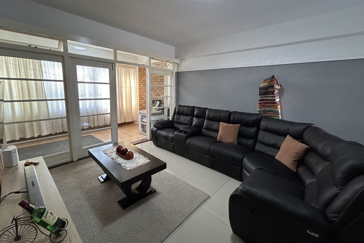 A spacious living room featuring tiled floors and large glass panel doors leading to an enclosed balcony area with exposed brick accents.