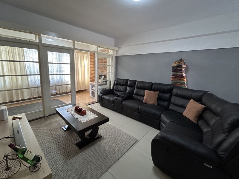A spacious living room featuring tiled floors and large glass panel doors leading to an enclosed balcony area with exposed brick accents.