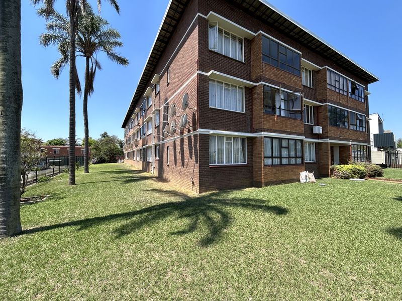 Exterior view of a multi-story brick apartment building featuring metal window frames, multiple satellite dishes, and surrounding communal lawn area.