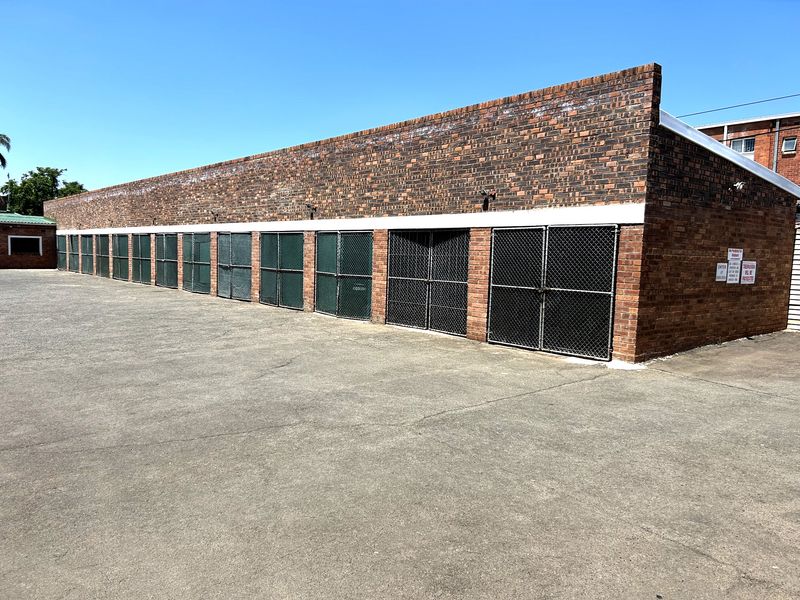 A row of secure, brick-constructed garage units featuring chain-link gates and a large concrete forecourt area.