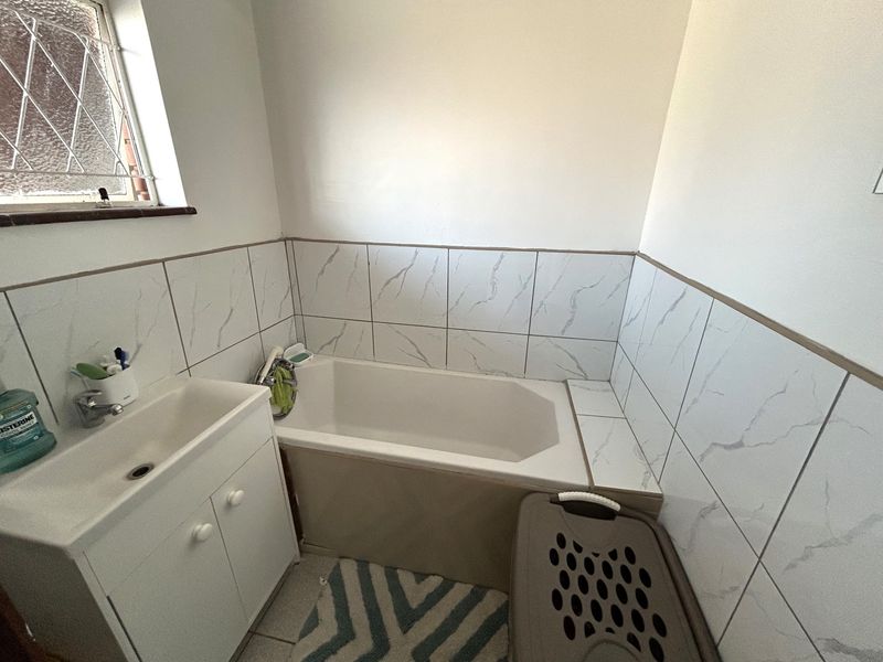 A functional bathroom featuring a built-in bathtub, vanity cabinet with basin, and marble-effect wall tiling.