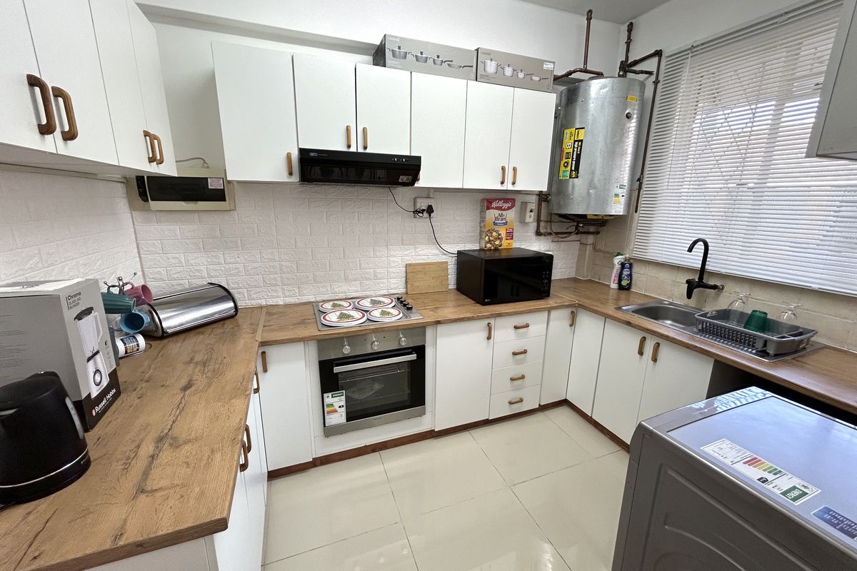 A functional kitchen featuring white cabinetry, wood-look laminate countertops, built-in oven and hob, and an exposed electric water heater.