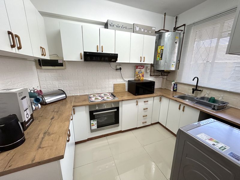 A functional kitchen featuring white cabinetry, wood-look laminate countertops, built-in oven and hob, and an exposed electric water heater.