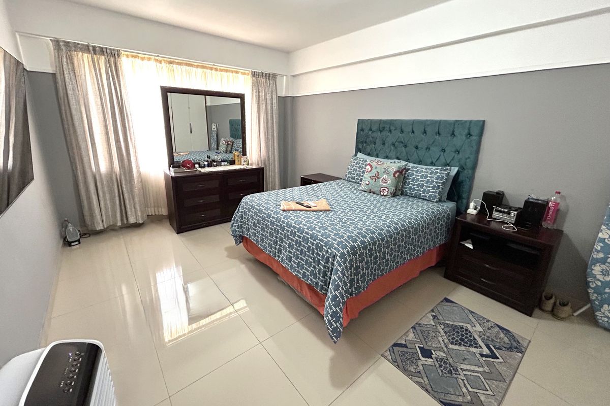 A spacious bedroom featuring neutral grey walls, large windows with curtains, and polished tiled flooring.