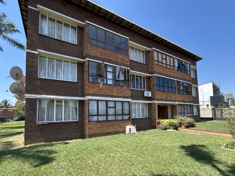 Exterior view of a multi-story brick apartment building featuring metal-framed windows and surrounding communal garden space.