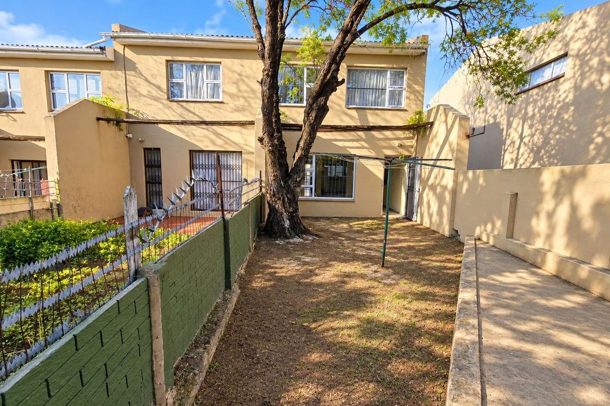 Rear view of the apartment featuring a private garden area, paved walkway, boundary wall with security spikes, and established tree.