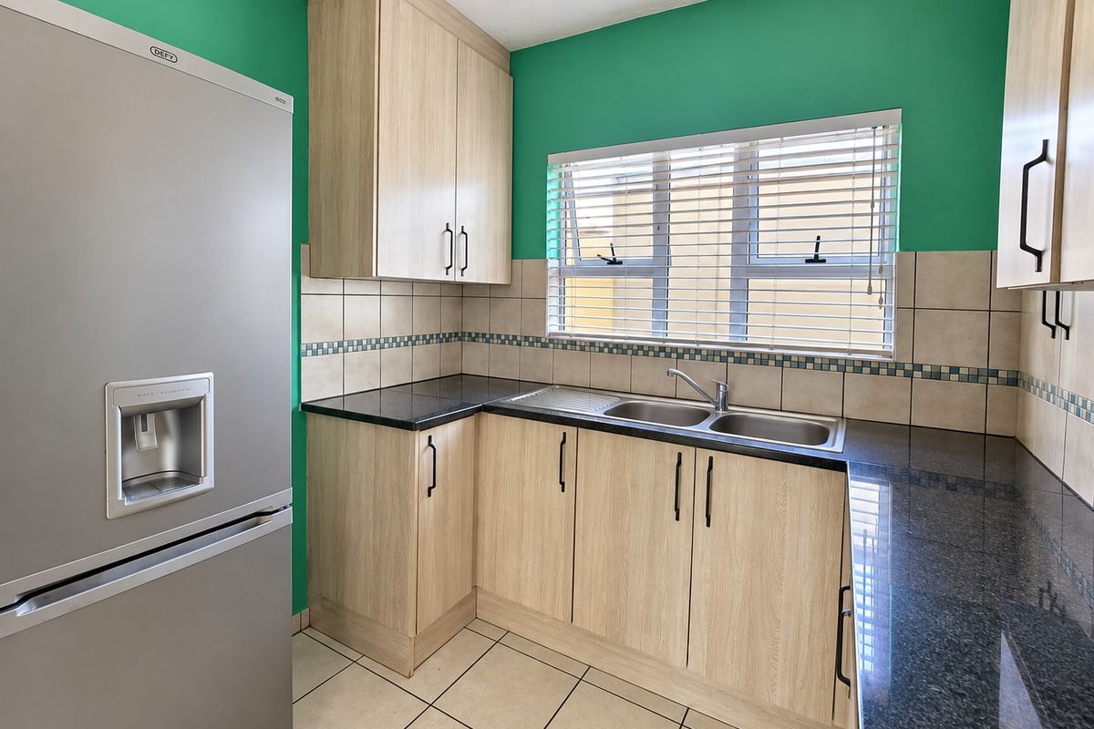 A functional kitchen featuring light wood-finish cabinetry, dark granite countertops, a stainless steel double sink, and tiled backsplash with a bright green accent wall.