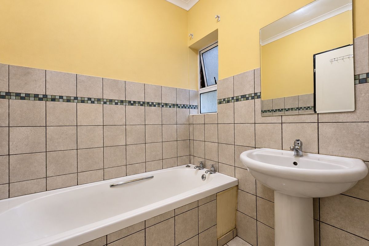 A functional bathroom featuring a bathtub, pedestal basin, and neutral wall tiling. The space is clean and ready for potential cosmetic updates.