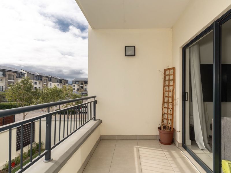 A clean, covered balcony featuring tiled flooring, a metal balustrade, and a sliding glass door providing access to the interior living space.