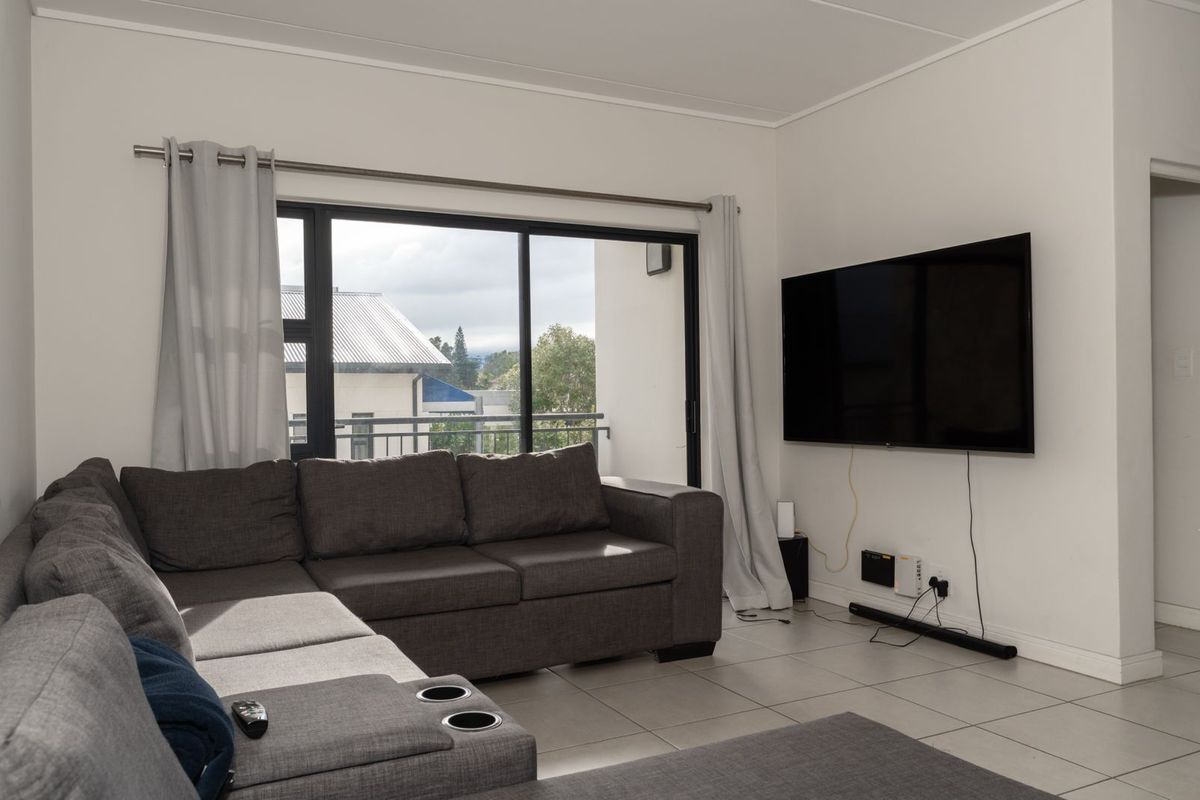 A bright living room featuring neutral tiled flooring, large sliding glass doors providing natural light, and a wall-mounted television setup.